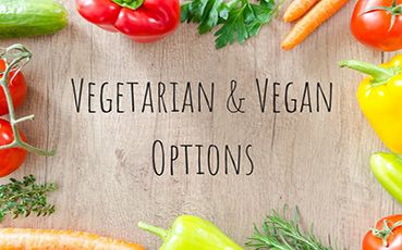 Brightly coloured fresh vegetables such as tomatoes, peppers, carrots, and herbs arranged around a light wooden surface showcasing vegetarian and vegan options at Thrive Childcare.
