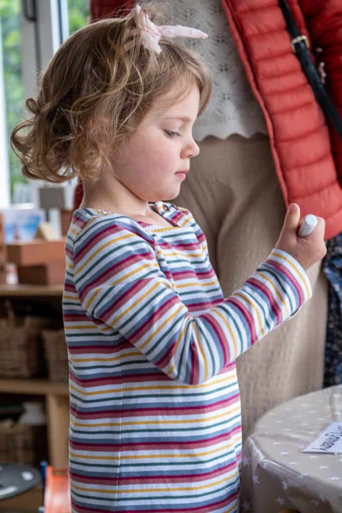 1. Young girl in colourful striped top writing or drawing with crayon at Thrive Childcare, engaging in creative activities for early childhood development.