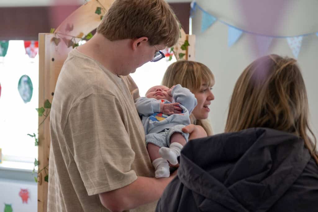 1. Friendly child caregiver holding a newborn baby in a colourful, welcoming childcare setting at Thrive Childcare.