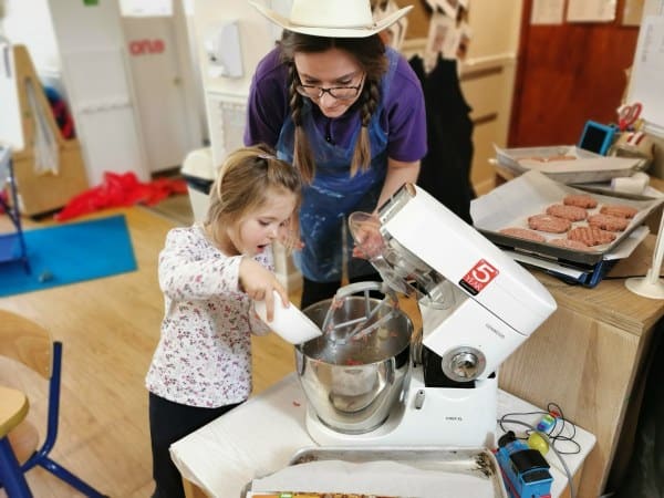 1. Young child and caregiver enjoying baking activity in a childcare setting, promoting early learning, creativity, and fun in a safe, nurturing environment.