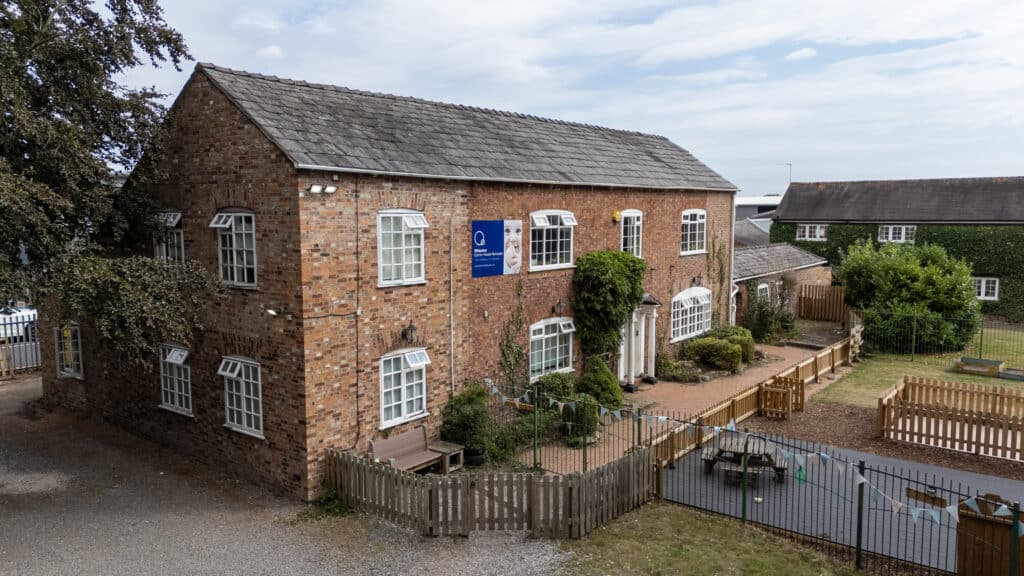 Bright brick-built Thrive Childcare centre with secure outdoor play area, surrounded by greenery and fencing, offering a safe environment for children's early learning and development.