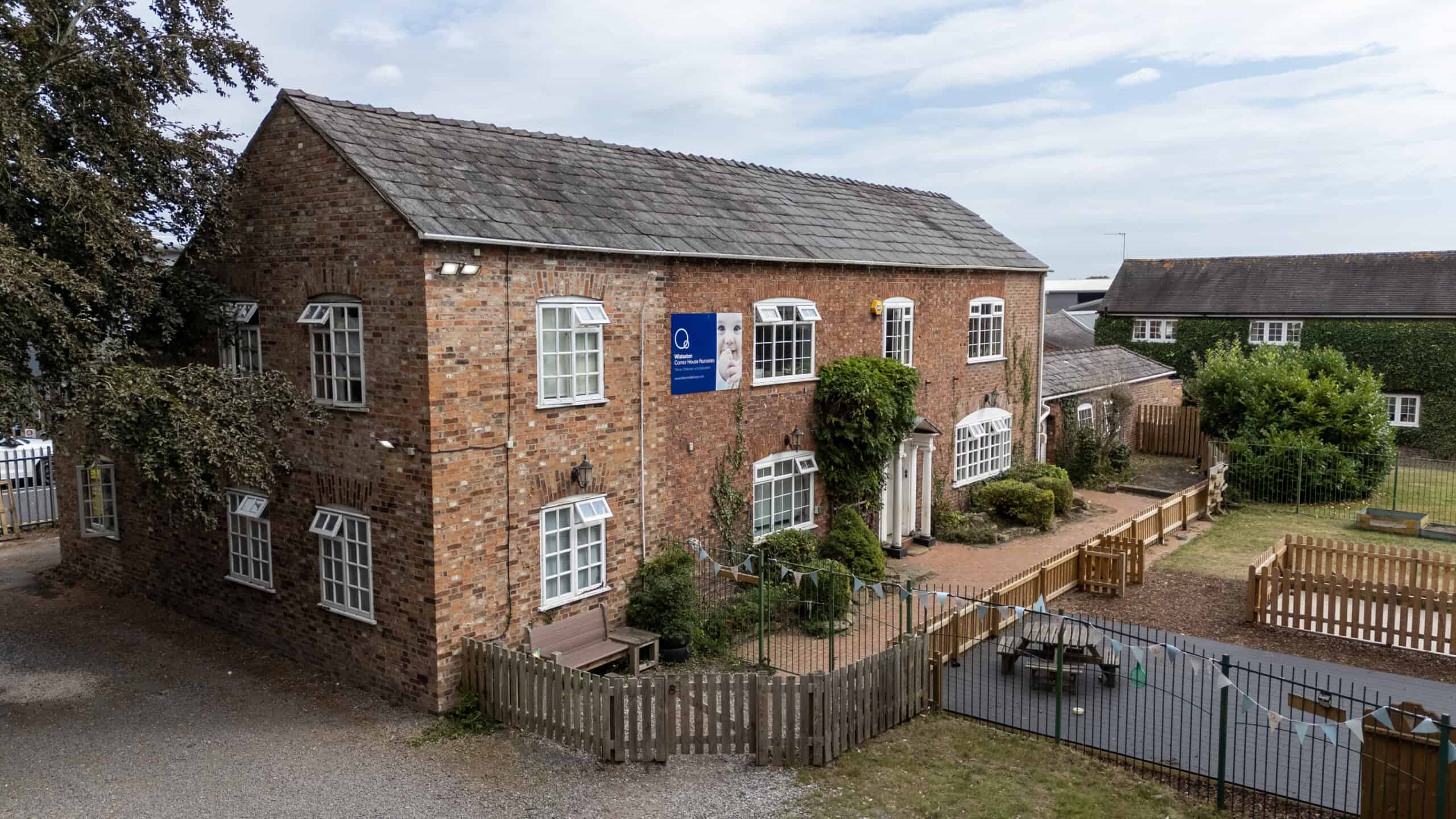 Bright brick-built Thrive Childcare centre with secure outdoor play area, surrounded by greenery and fencing, offering a safe environment for children's early learning and development.
