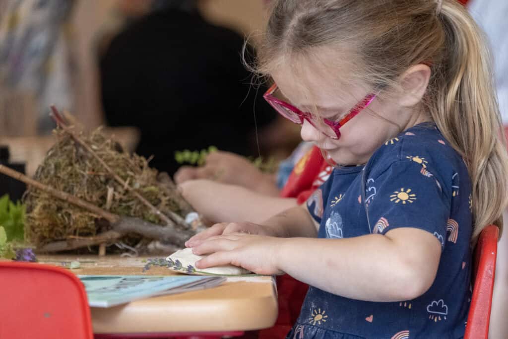 A young girl with red glasses engaging in hands-on creative activity at Thrive Childcare, focusing on early childhood development and play-based learning.