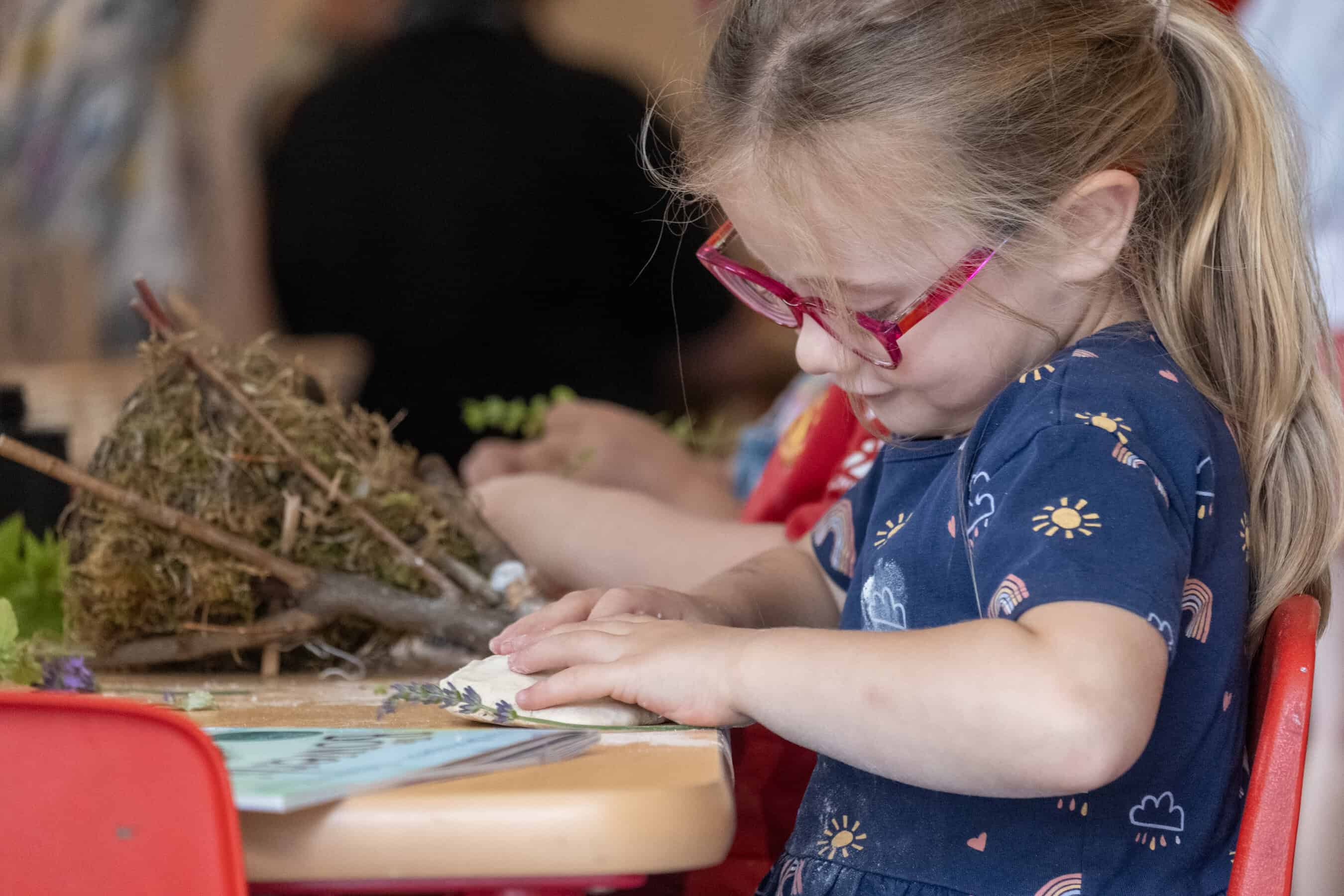 A young girl with red glasses engaging in hands-on creative activity at Thrive Childcare, focusing on early childhood development and play-based learning.