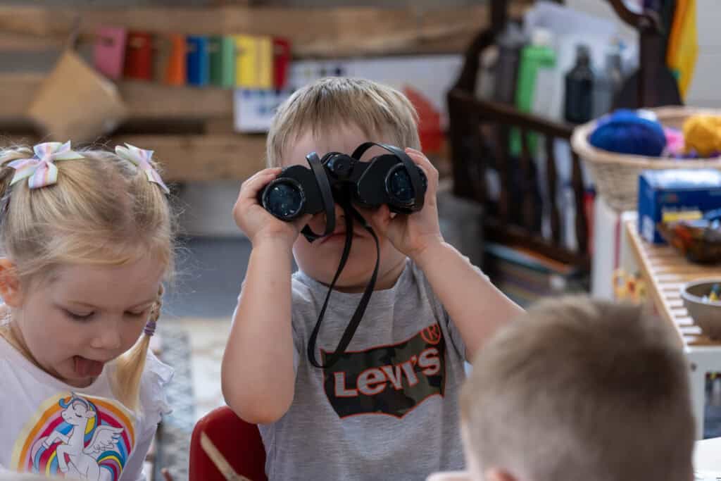 1. Kids at Thrive Childcare engaging in imaginative play with a child using binoculars in a colourful, nurturing preschool environment.