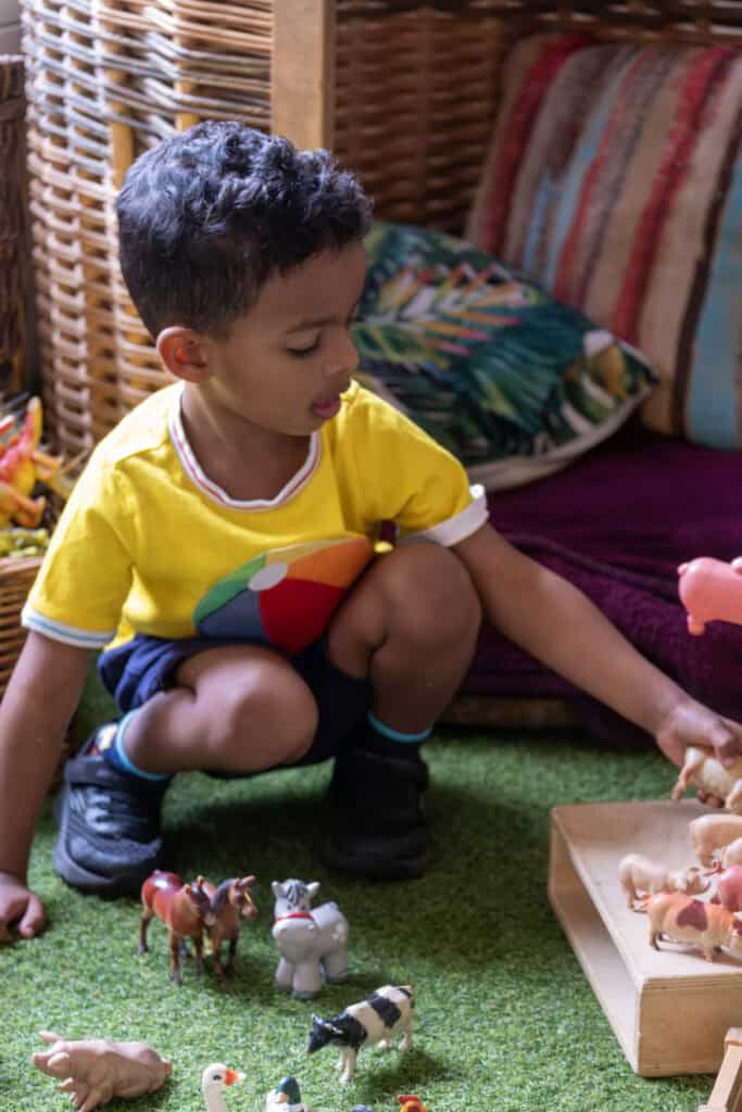 A young child playing with animal figurines on a green mat in a colourful indoor play area, promoting early childhood development and imaginative play at Thrive Childcare.
