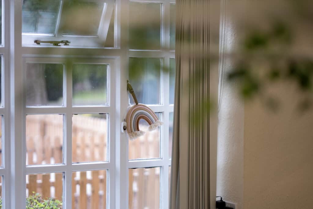 Bright children's nursery window with rainbow wall hanging, natural daylight, and view of outdoor garden at Thrive Childcare, creating a cheerful and nurturing environment for early childhood development.
