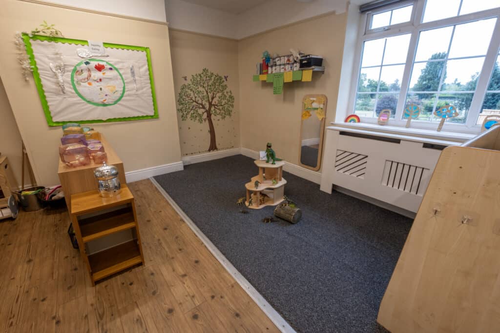 Bright childcare playroom with educational decor, wooden furniture, large window with scenic view, and themed decorations promoting a safe, engaging environment for young children at Thrive Childcare.