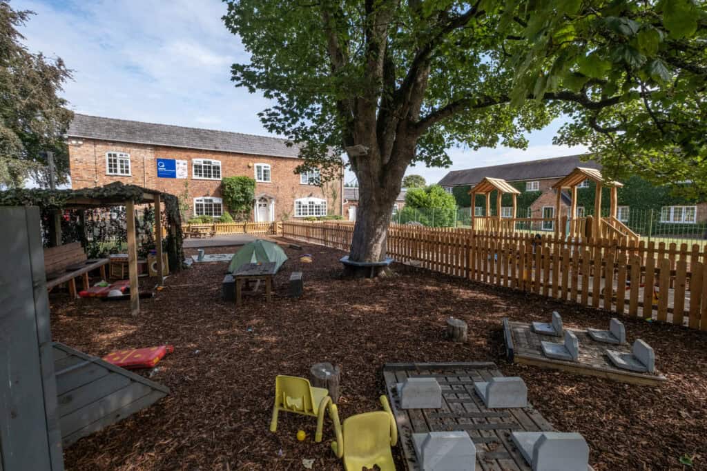 Bright outdoor childcare play area with wooden play structures, shaded picnic spots, and soft ground cover, ideal for facilitating child development and outdoor learning at Thrive Childcare.