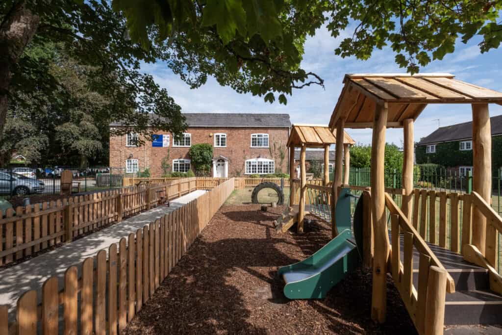 Vibrant outdoor play area at Thrive Childcare with wooden structures and slides, surrounded by a secure fence, providing a safe, fun environment for children's outdoor activities and development.