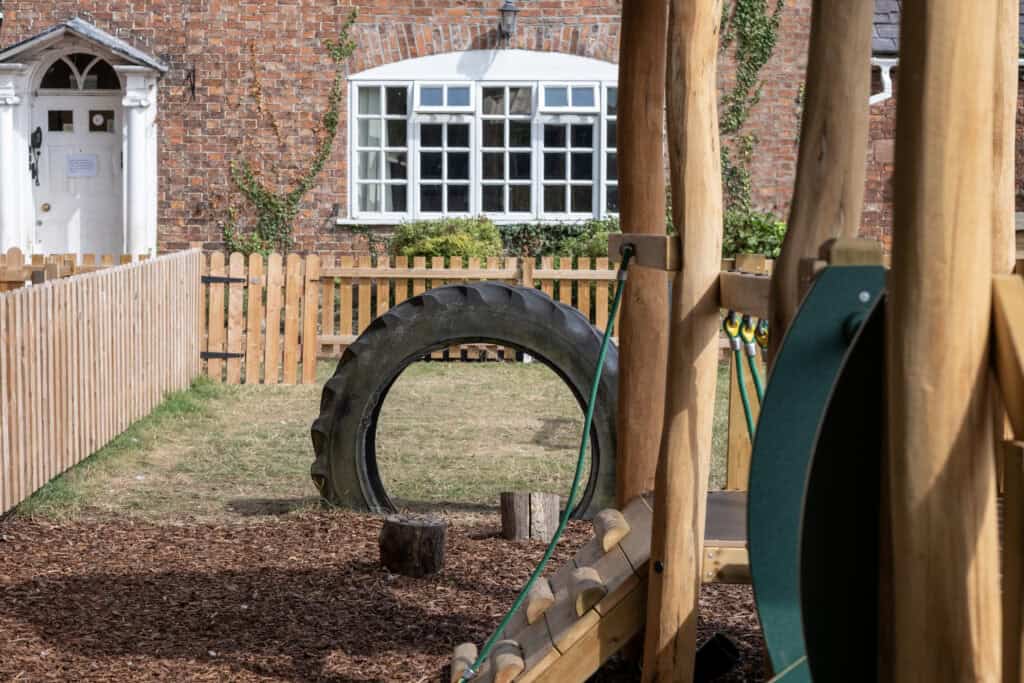 Bright outdoor playground at Thrive Childcare featuring a large tire swing, wooden climbing structures, and a safe fenced area for children’s play and physical development.
