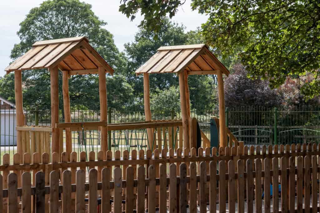 Wooden outdoor playhouse structures at Thrive Childcare with green trees in the background, perfect for early childhood development, outdoor activities, and quality childcare environments.