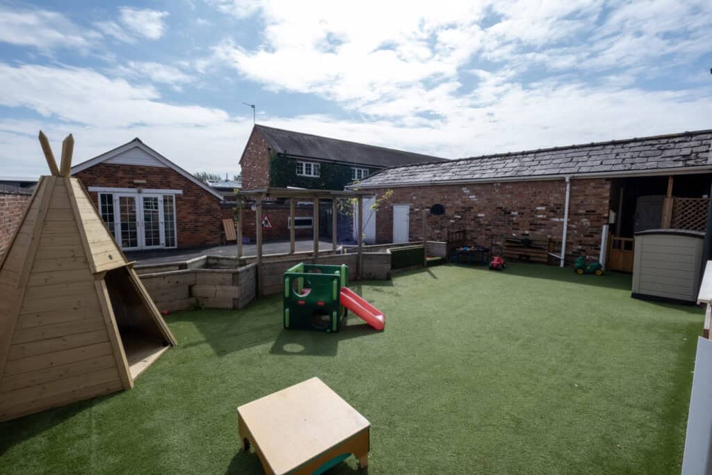 Bright outdoor play area at Thrive Childcare with artificial grass, wooden playhouses, colourful toys, and safe climbing structures for children's outdoor activities and development.