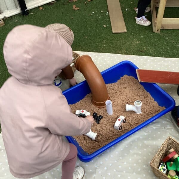Child playing with a sensory sand and pipe play set at Thrive Childcare, encouraging imaginative and tactile development outdoors.