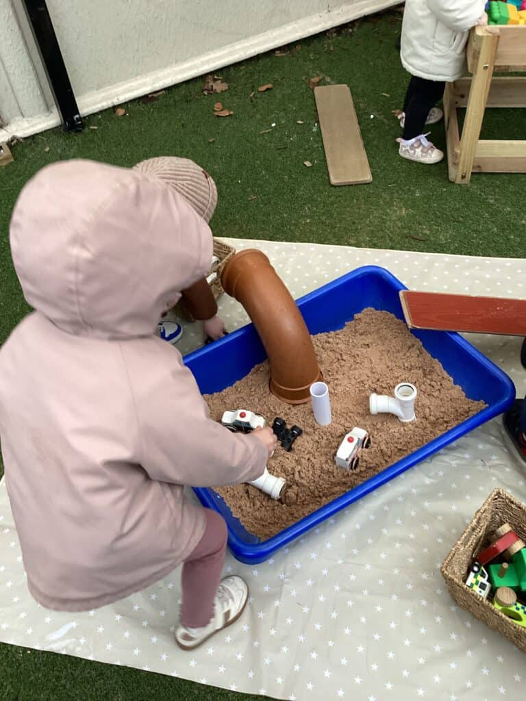 Child playing with a sensory sand and pipe play set at Thrive Childcare, encouraging imaginative and tactile development outdoors.