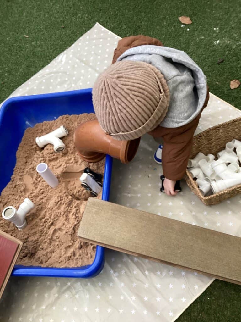 A child playing in a sand and water play area at Thrive Childcare, engaging with pipes and sand toys for sensory development and outdoor fun.