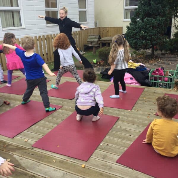 Children's outdoor yoga session at Thrive Childcare centre in a garden setting with an instructor guiding kids in exercise activities.