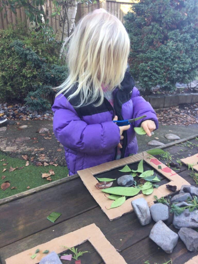 Bright preschool child engaging in outdoor nature activities at Thrive Childcare, exploring leaves, stones, and natural materials in a garden setting for early childhood development.