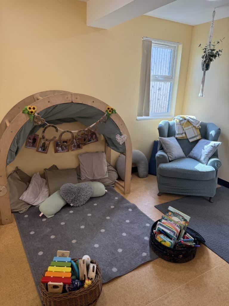 Soft play area in nursery with cushions, a hanging chair, and children's books, creating a warm and inviting learning environment at Thrive Childcare.