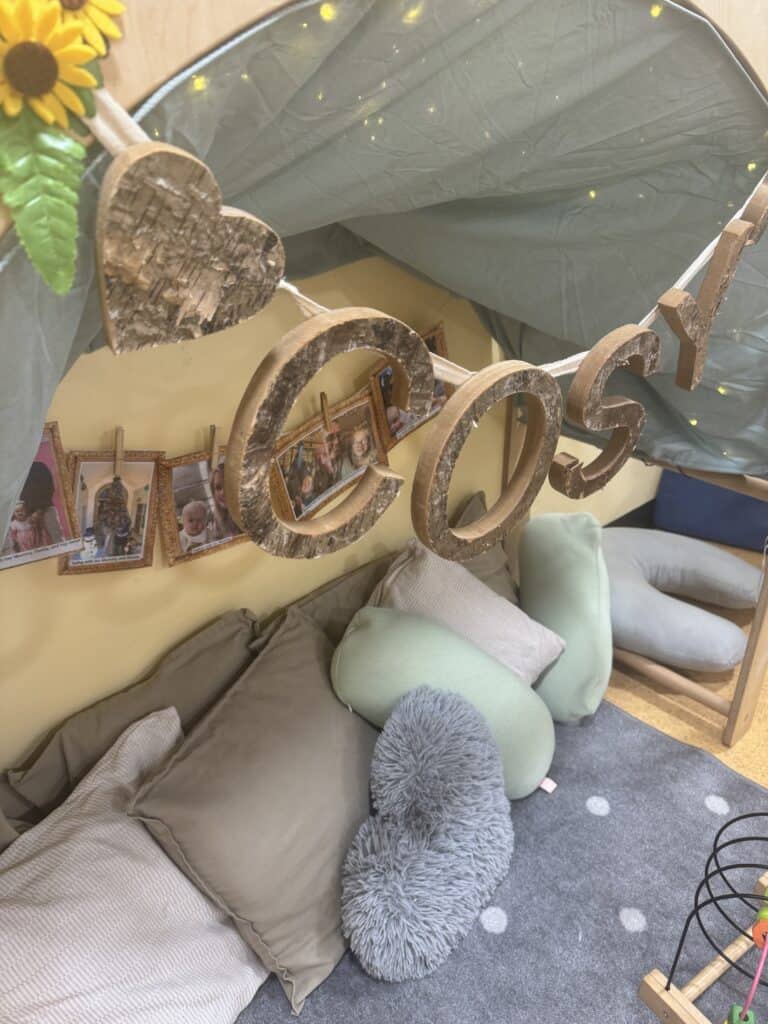 Warm, inviting childcare indoor play area with cozy cushions, wooden heart decor, and personalised photo garland, creating a safe and nurturing environment for young children at Thrive Childcare.