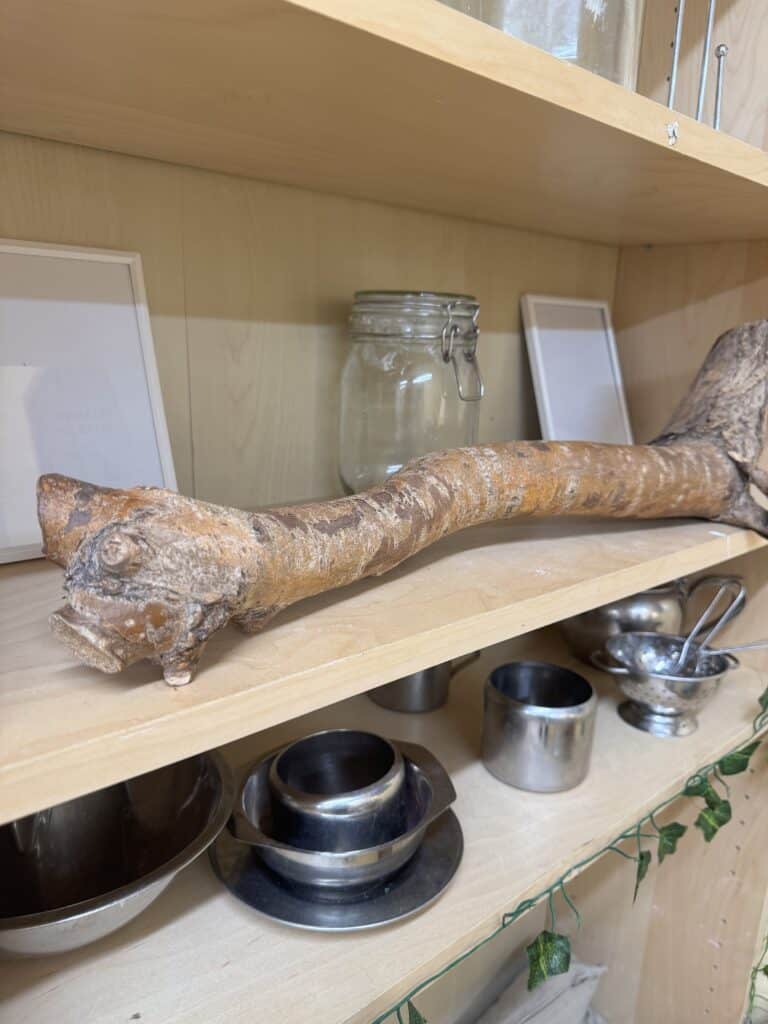A wooden shelf with a branch, jars, and metal bowls, part of Thrive Childcare's natural and eco-friendly learning environment for children.