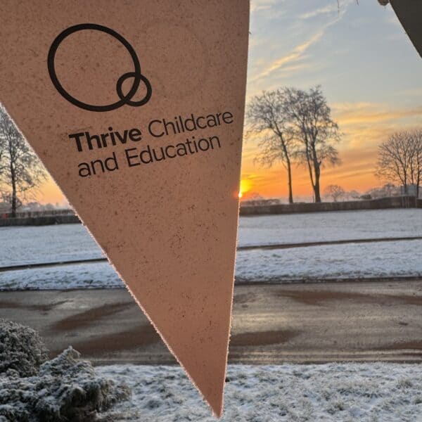 Bright pink Thrive Childcare and Education banner flying outdoors at sunset, with winter landscape and snow-covered ground and trees, promoting childcare and early education services.
