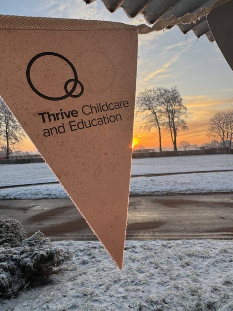 Bright pink Thrive Childcare and Education banner flying outdoors at sunset, with winter landscape and snow-covered ground and trees, promoting childcare and early education services.