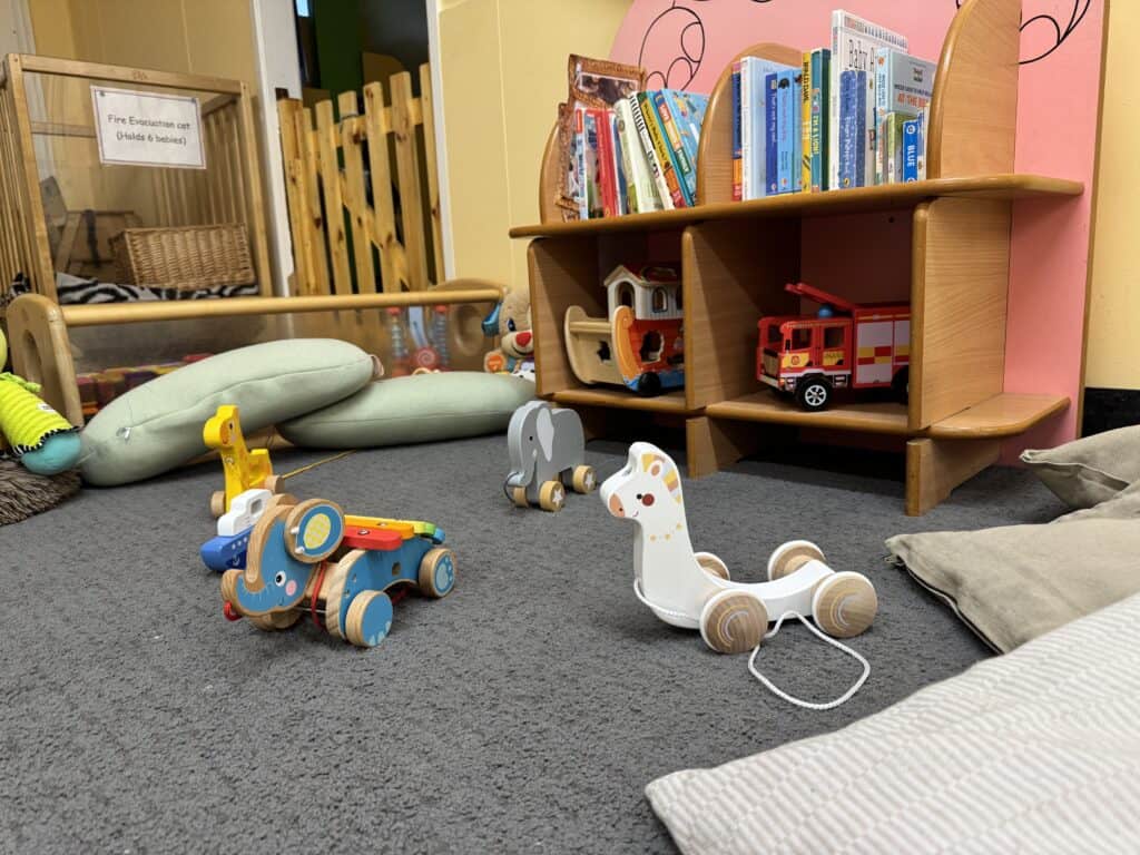 Bright, safe, and engaging children's play area at Thrive Childcare featuring wooden animal ride-on toys, soft cushions, and a colourful book display for early childhood development and learning.