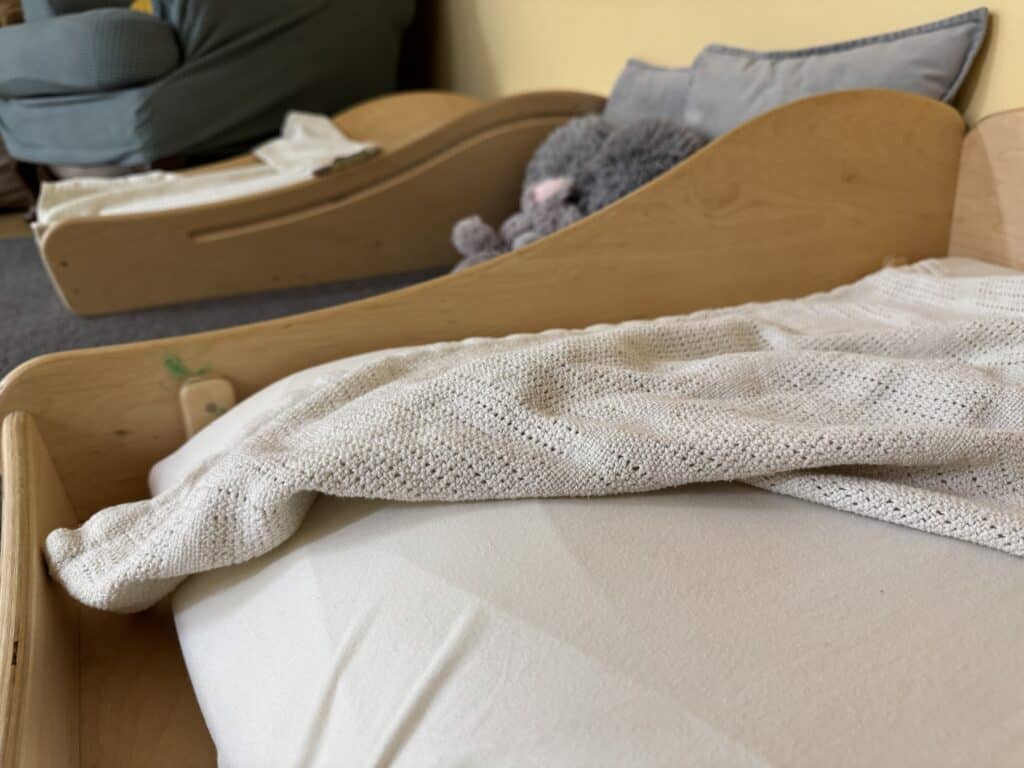 Softly made wooden cots with cozy blankets for babies and young children in a warm, welcoming nursery at Thrive Childcare. Comfortable and safe sleeping environment promoting early childhood development.