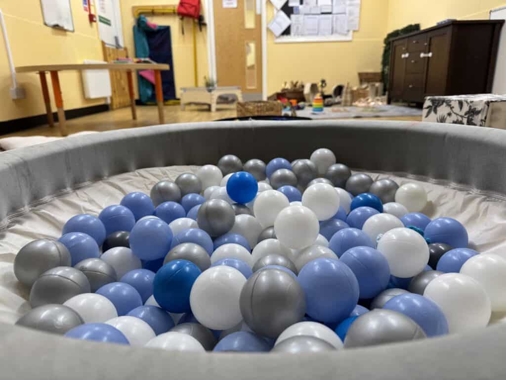 Bright indoor childcare play area with a ball pit filled with colourful blue, white, and grey plastic balls, promoting fun and sensory development for young children.