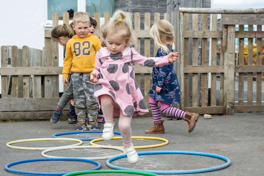 Bright preschool children playing and hopping through colourful hoops outdoors at Thrive Childcare, promoting early childhood development, social skills, and outdoor learning.
