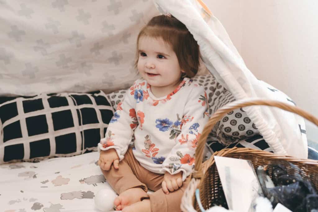 1. Young toddler girl sitting on a bed in a nursery, engaging in early childhood development activities at Thrive Childcare, with a focus on nurturing care and learning environments.