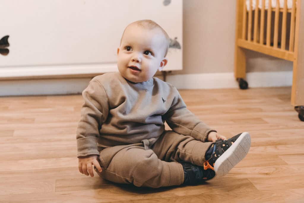 Soft toy toddler sitting on wooden floor at Thrive Childcare, early childhood education, childcare service, happy child playing, nurturing environment for young kids, safe and engaging nursery setting, toddler development, quality childcare UK.