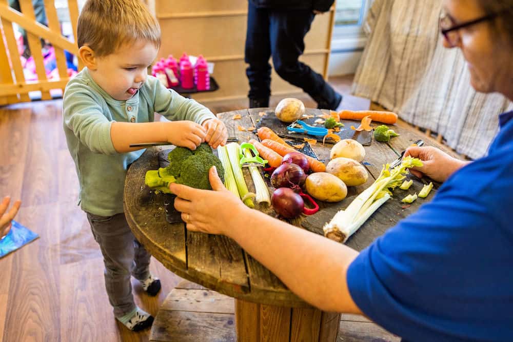 Broccoli and vegetables on a table with a young child and adult engaging in healthy food activity in a childcare setting.