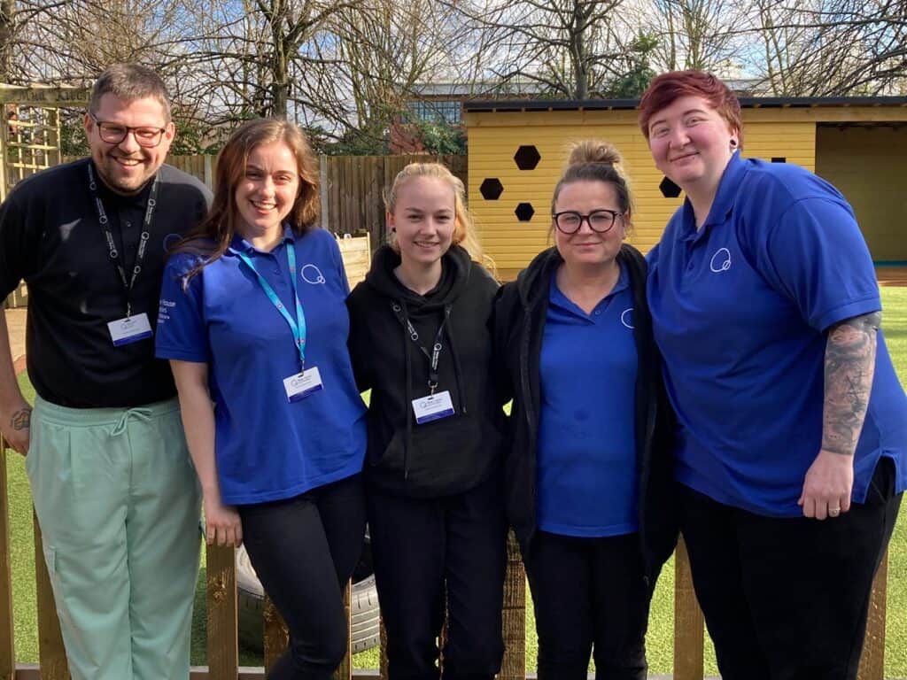 Caring childcare staff team at Thrive Childcare, smiling outdoors in uniform, showcasing dedication to early childhood education and nurturing environments for children's development.