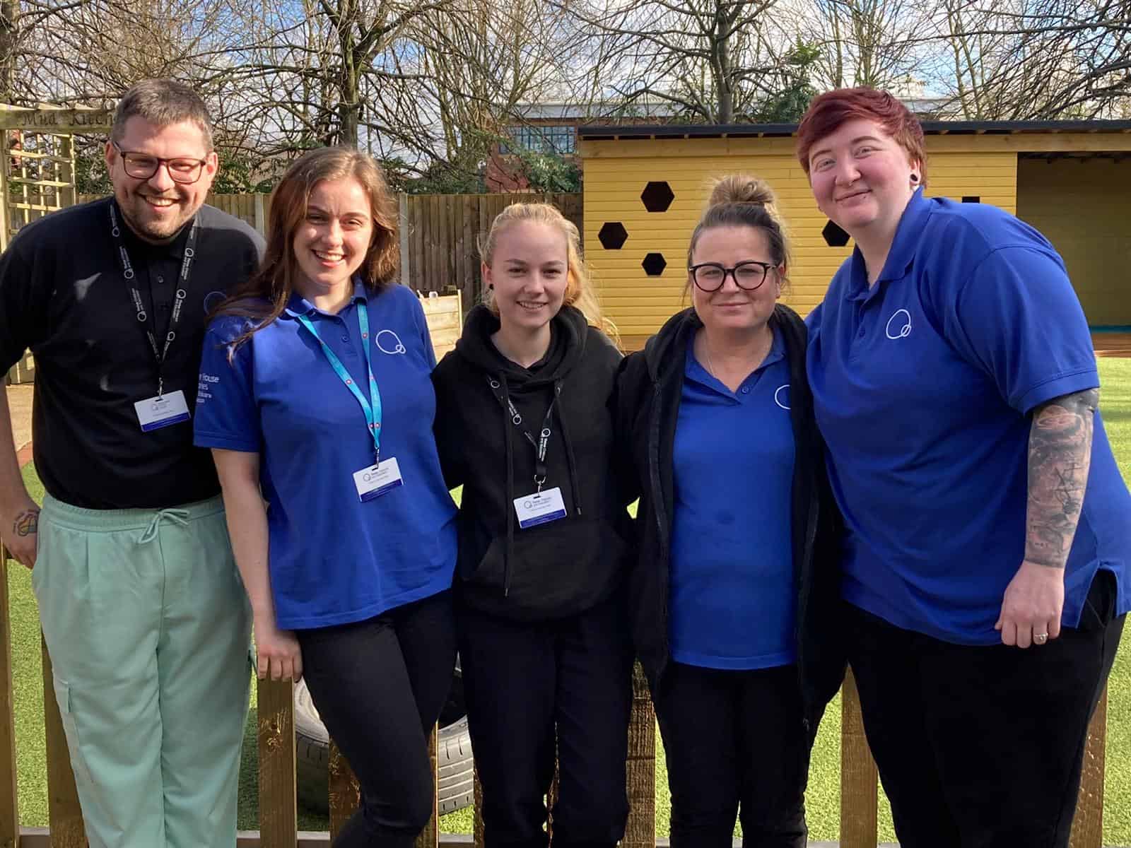Caring childcare staff team at Thrive Childcare, smiling outdoors in uniform, showcasing dedication to early childhood education and nurturing environments for children's development.