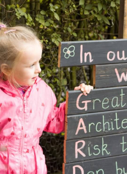 Childcare outdoor learning environment at Thrive Childcare featuring a young girl with a chalkboard sign promoting positive values and early childhood development.