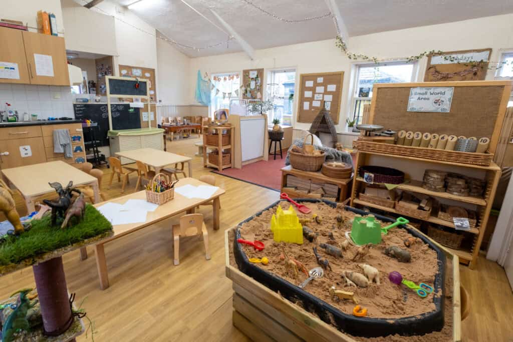 Bright indoor nursery play area with sandpit, wooden furniture, toys, and educational displays, ideal for early childhood development and child care services at Thrive Childcare.