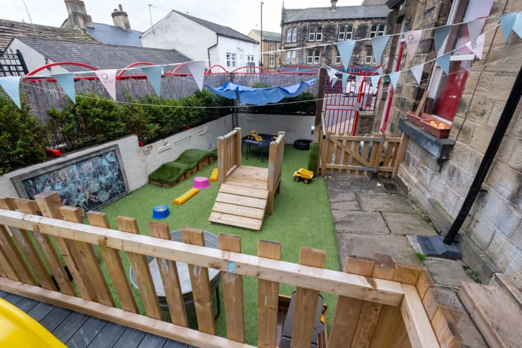 Bright outdoor play area at Thrive Childcare with safety fencing, play equipment, and artificial grass, ideal for early childhood development and fun in a secure environment.
