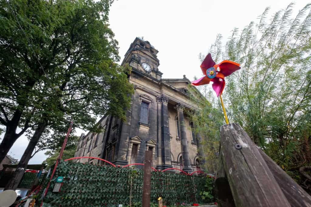Colourful windmill sculpture in a children's playground with historic church in the background, showcasing vibrant outdoor play area at Thrive Childcare, a trusted local childcare provider.