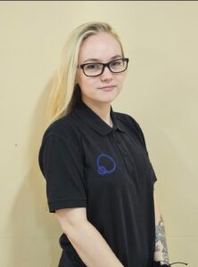 Caring childcare staff member at Thrive Childcare, wearing a uniform with social and emotional development focus, indoors against neutral background.