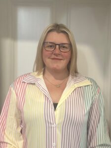 Supportive childcare professional at Thrive Childcare centre, smiling confidently in colourful striped shirt, committed to child development and quality early years education.