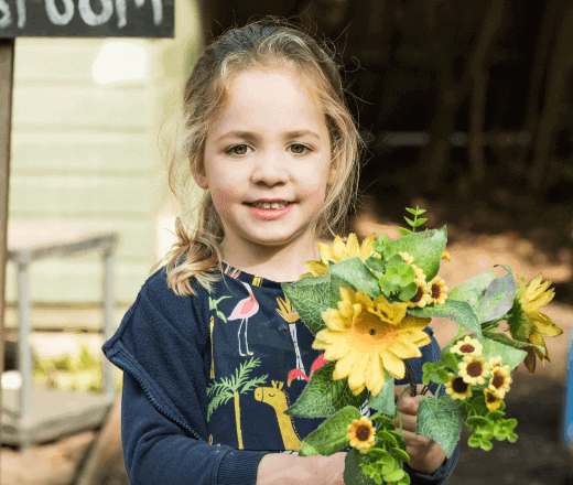 A young girl holding a vibrant sunflower and greenery at Thrive Childcare, showcasing a nurturing environment and outdoor activities for early childhood development.