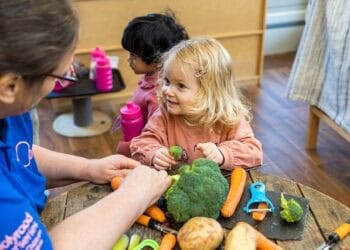 Bright-eyed children enjoy a playful activity with a caregiver at Thrive Childcare, engaging in hands-on learning and crafting, fostering development and fun in a safe, nurturing environment.