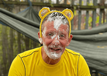 A happy man with a yellow bear ear headband and foam on his face, enjoying playful activities outdoors at Thrive Childcare.