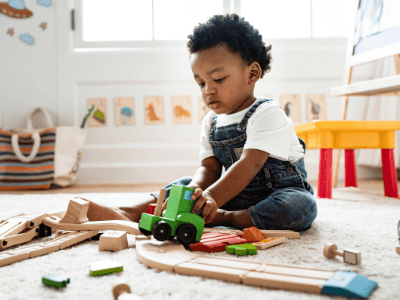 A young child playing with wooden train toys in a safe, colourful childcare environment at Thrive Childcare, promoting early childhood development and playful learning.