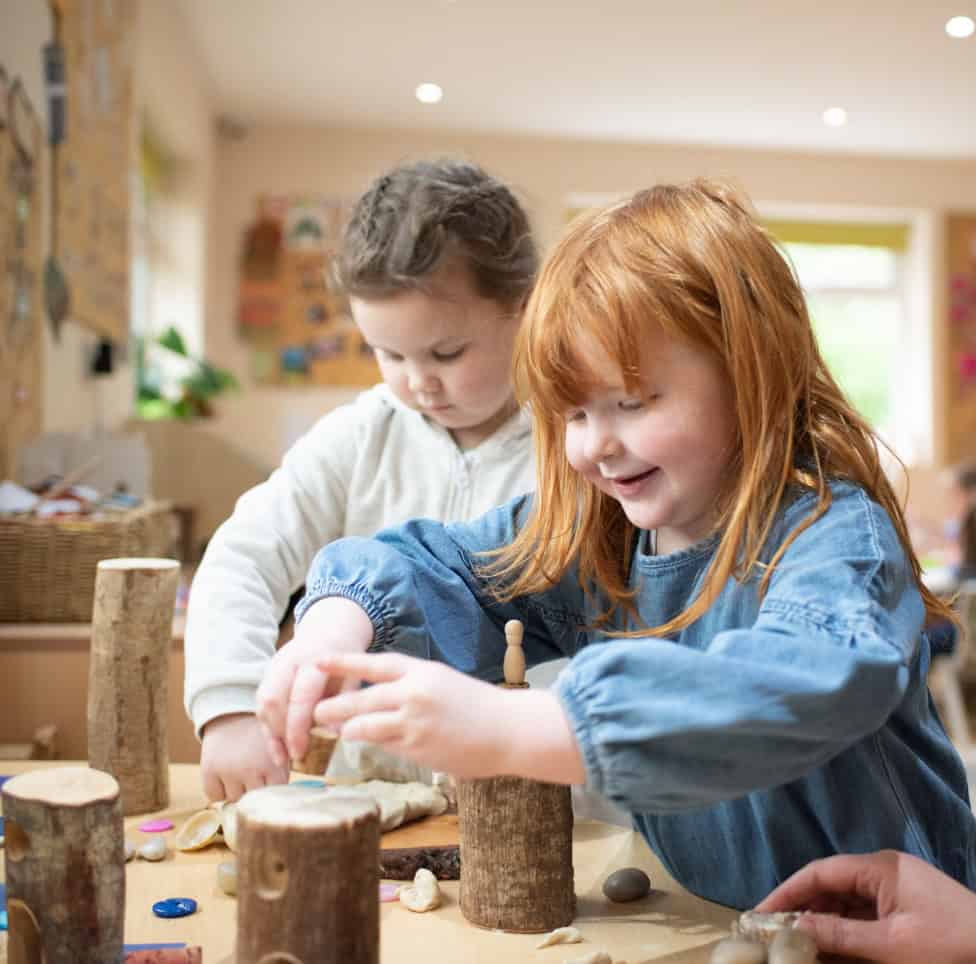 1. Two young children playing creatively with wooden logs and natural materials in a bright, welcoming childcare setting at Thrive Childcare.