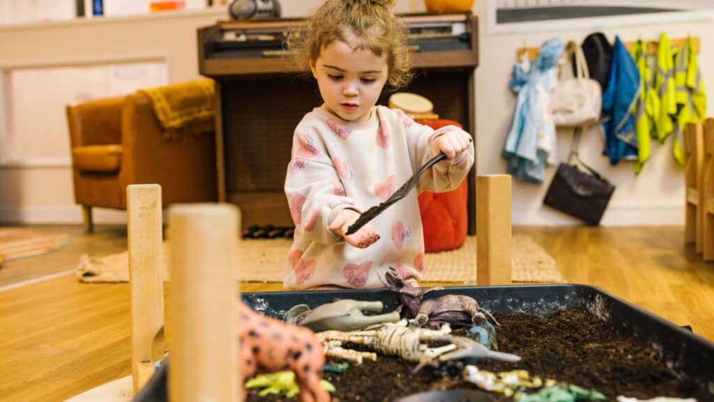 Bright-eyed toddler engaging in imaginative play with plastic animal figurines in a colourful nursery setting at Thrive Childcare.
