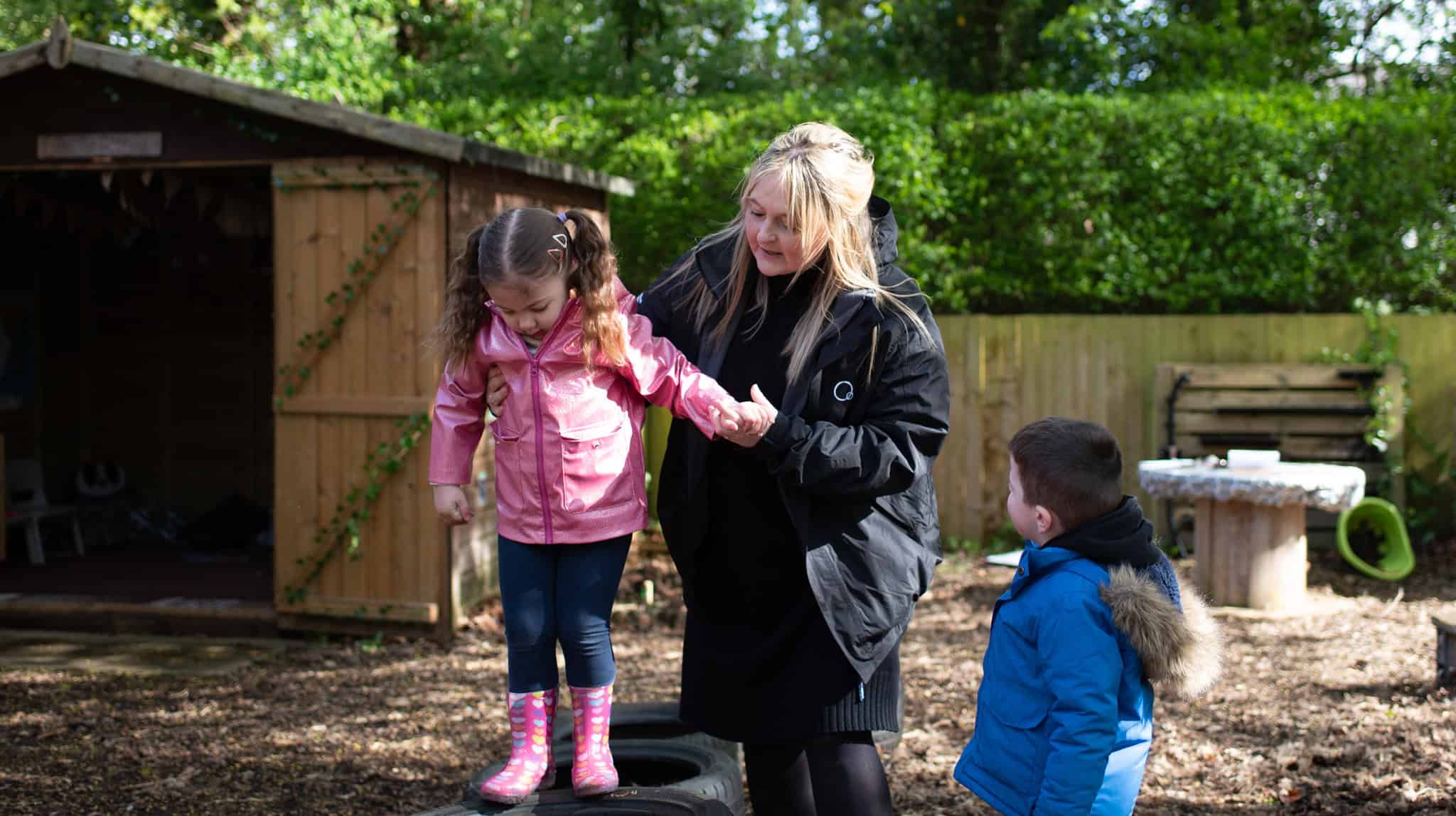 Energetic young girl balancing on a tyre obstacle at Thrive Childcare outdoor play area with teacher supervision.