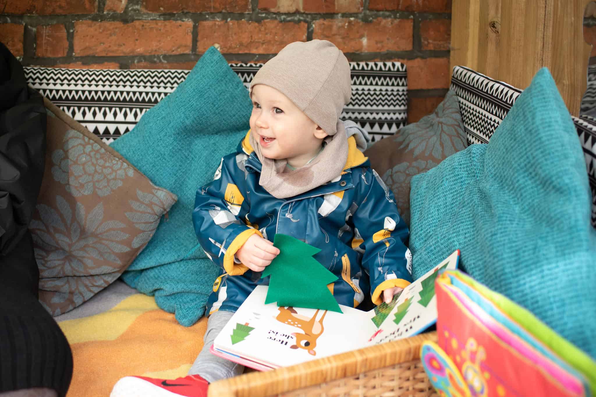 1. A young child in colourful raincoat and beanie enjoying storytime at Thrive Childcare indoors.
